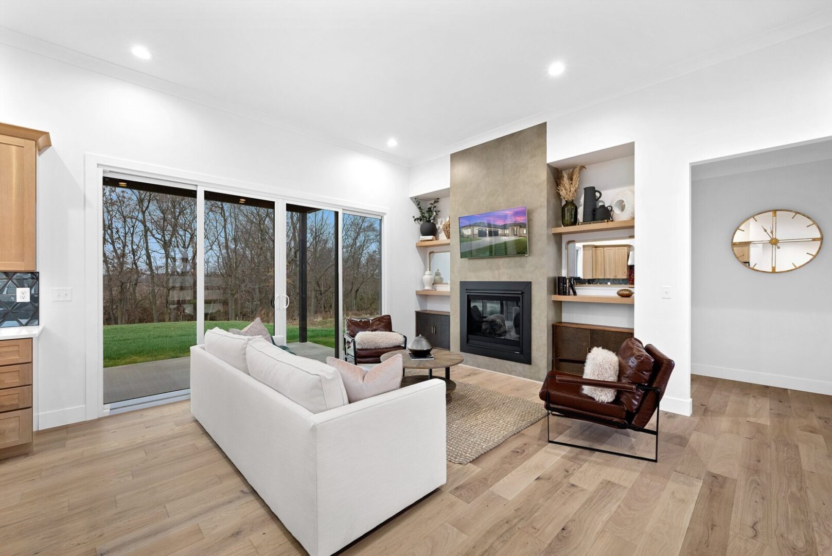 The design features an open floor plan with a spacious great room, complete with a faux concrete fireplace, white oak floating shelves, and a sliding glass door leading to a covered patio.