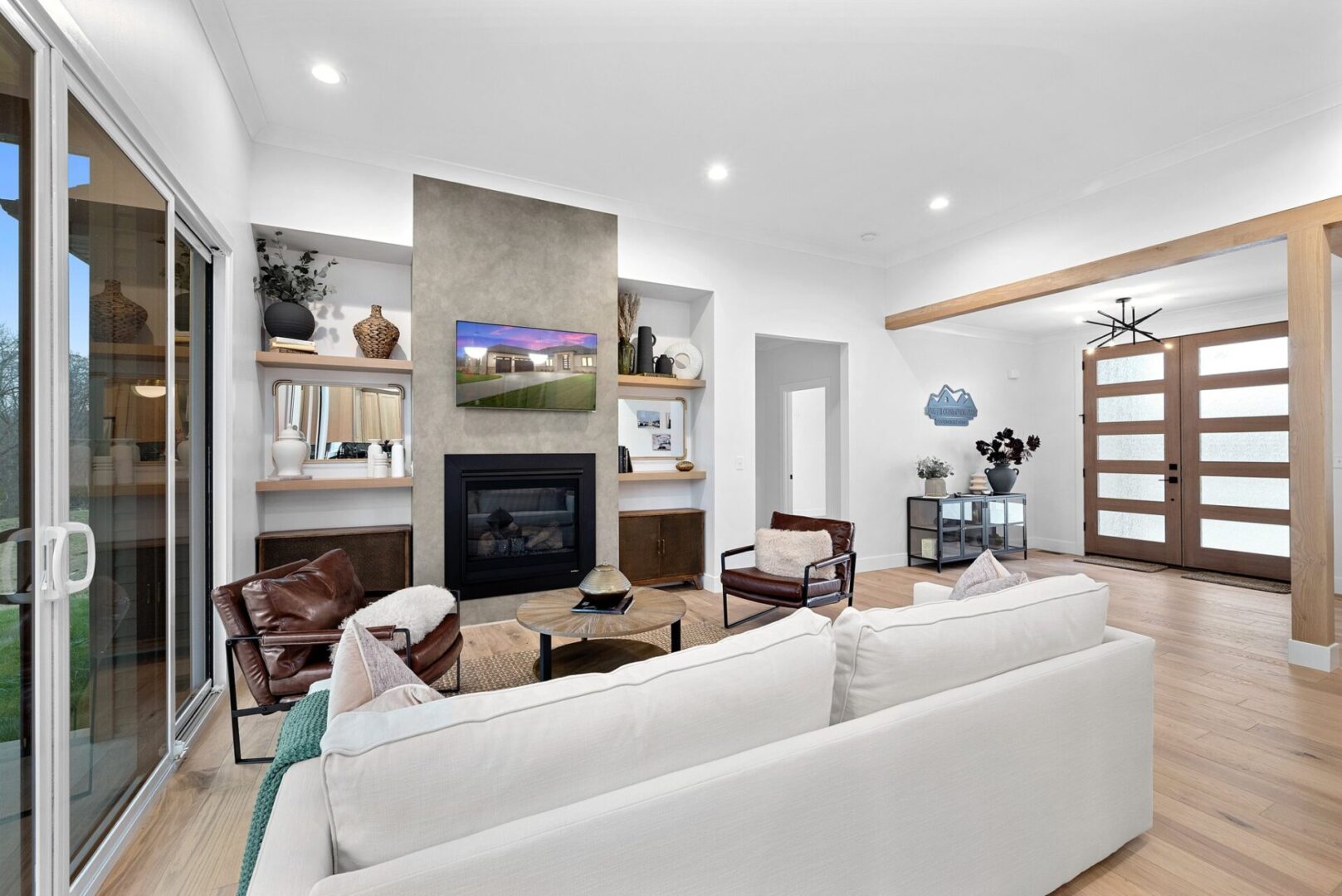 The design features an open floor plan with a spacious great room, complete with a faux concrete fireplace, white oak floating shelves, and a sliding glass door leading to a covered patio.