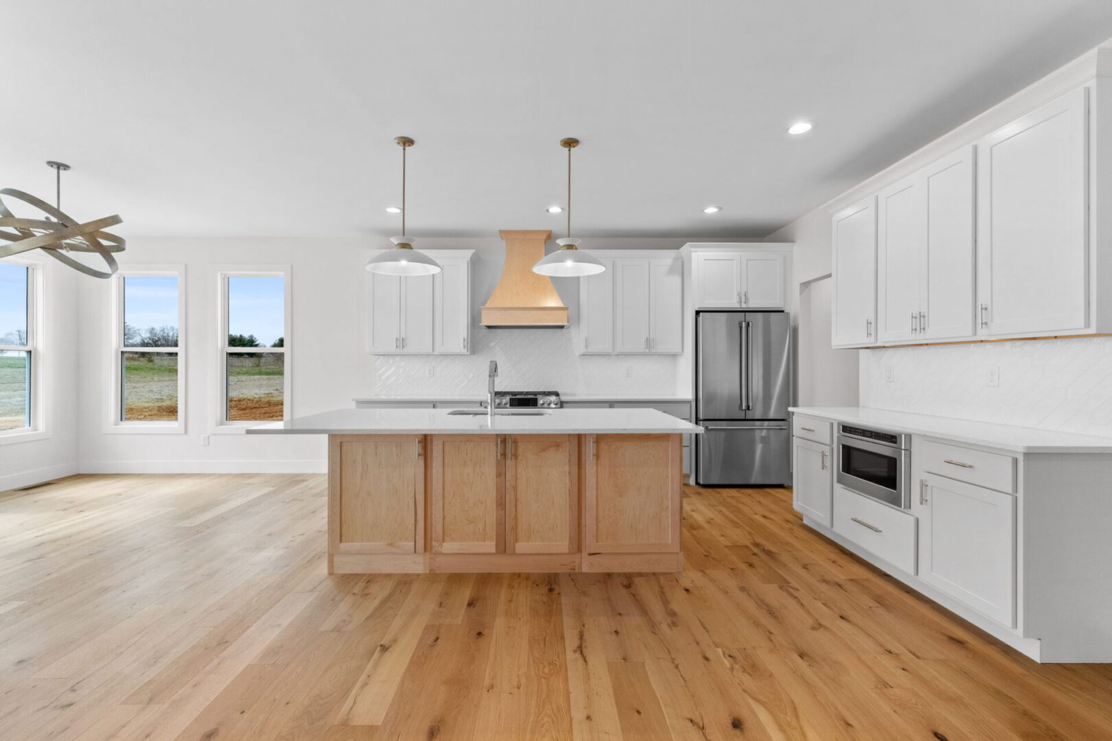 The kitchen showcases a contemporary design featuring custom Aspect cabinetry and quartz countertops, complemented by Café stainless steel appliances. It highlights a wooden bodice-shaped hood vent and modern dome lighting, all revolving around an impressive white oak island. The white diagonal picket tile backsplash adds a modern elegance to this contemporary and clean kitchen.