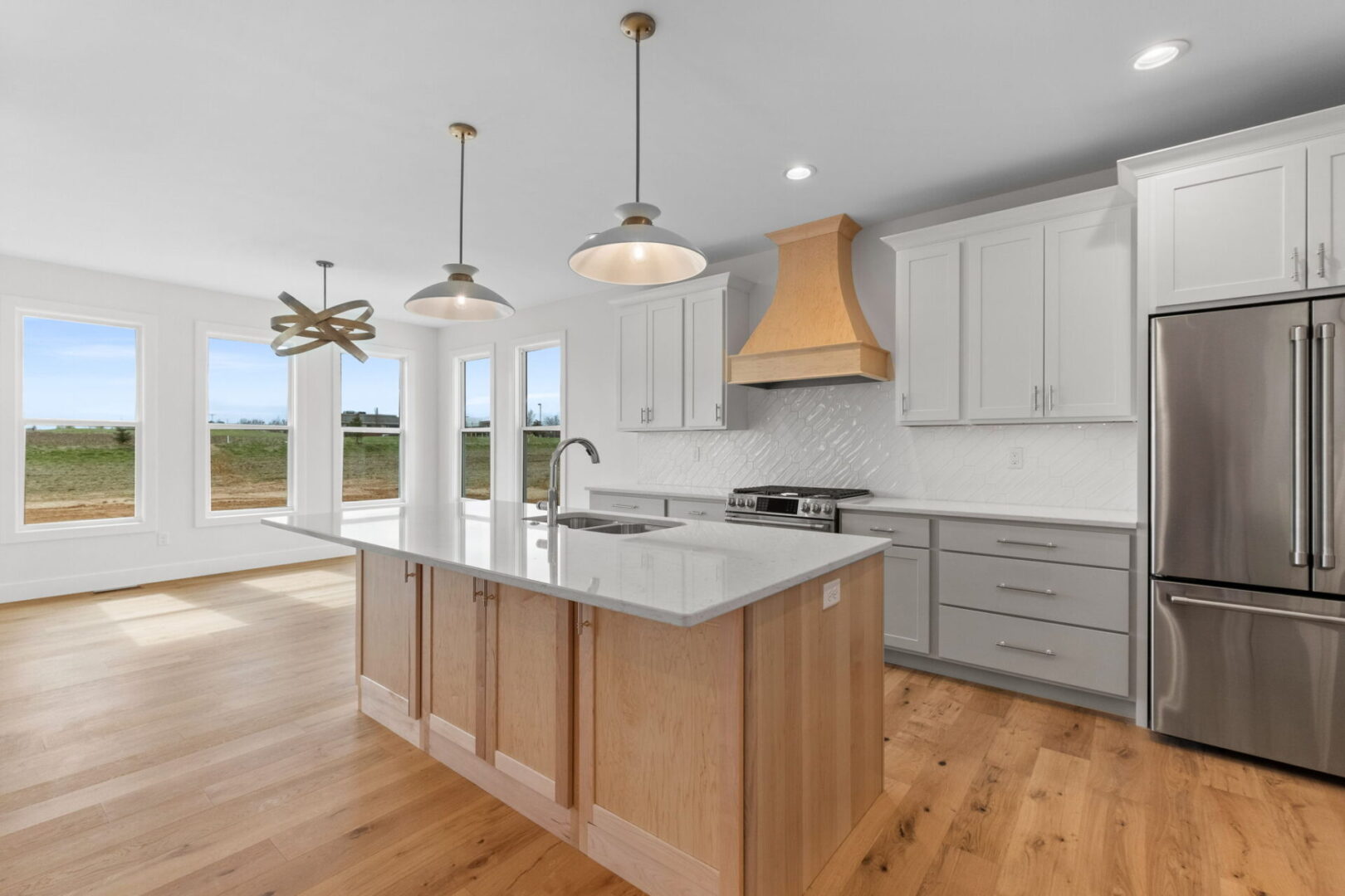 The kitchen showcases a contemporary design featuring custom Aspect cabinetry and quartz countertops, complemented by Café stainless steel appliances. It highlights a wooden bodice-shaped hood vent and modern dome lighting, all revolving around an impressive white oak island. The white diagonal picket tile backsplash adds a modern elegance to this contemporary and clean kitchen.