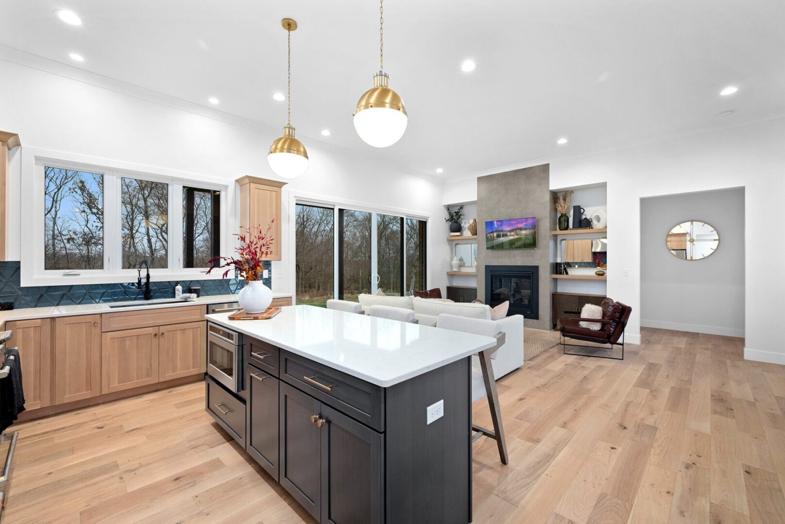 The kitchen boasts a modern design white oak with custom Shiloh cabinets and quartz countertops, paired with Cafe' stainless steel appliances. It features a bodice-shaped hood vent and contemporary dome lighting, all centered around a stunning navy hale island. Faux concrete fireplace and white oak floating shelves.