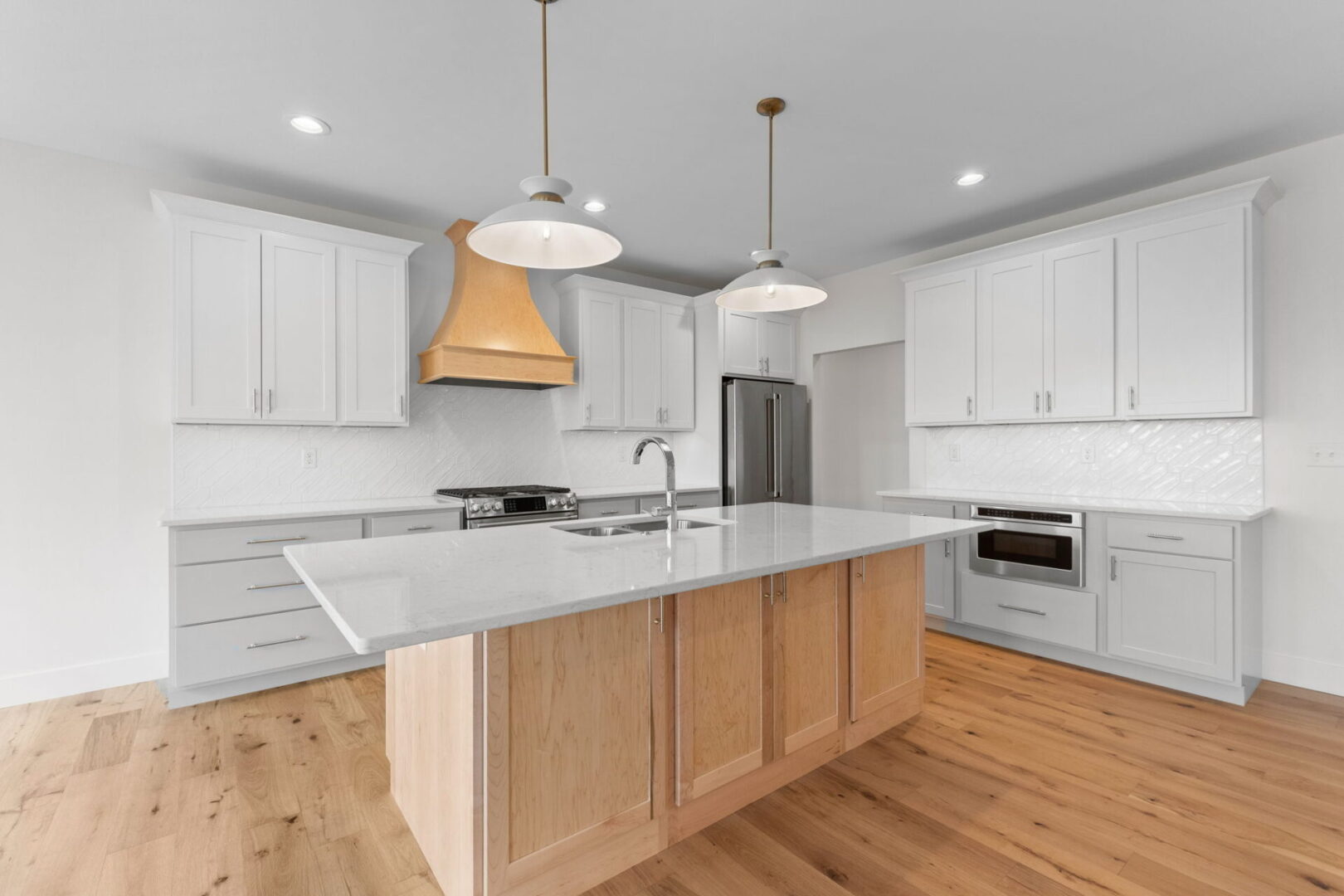The kitchen showcases a contemporary design featuring custom Aspect cabinetry and quartz countertops, complemented by Café stainless steel appliances. It highlights a wooden bodice-shaped hood vent and modern dome lighting, all revolving around an impressive white oak island. The white diagonal picket tile backsplash adds a modern elegance to this contemporary and clean kitchen.