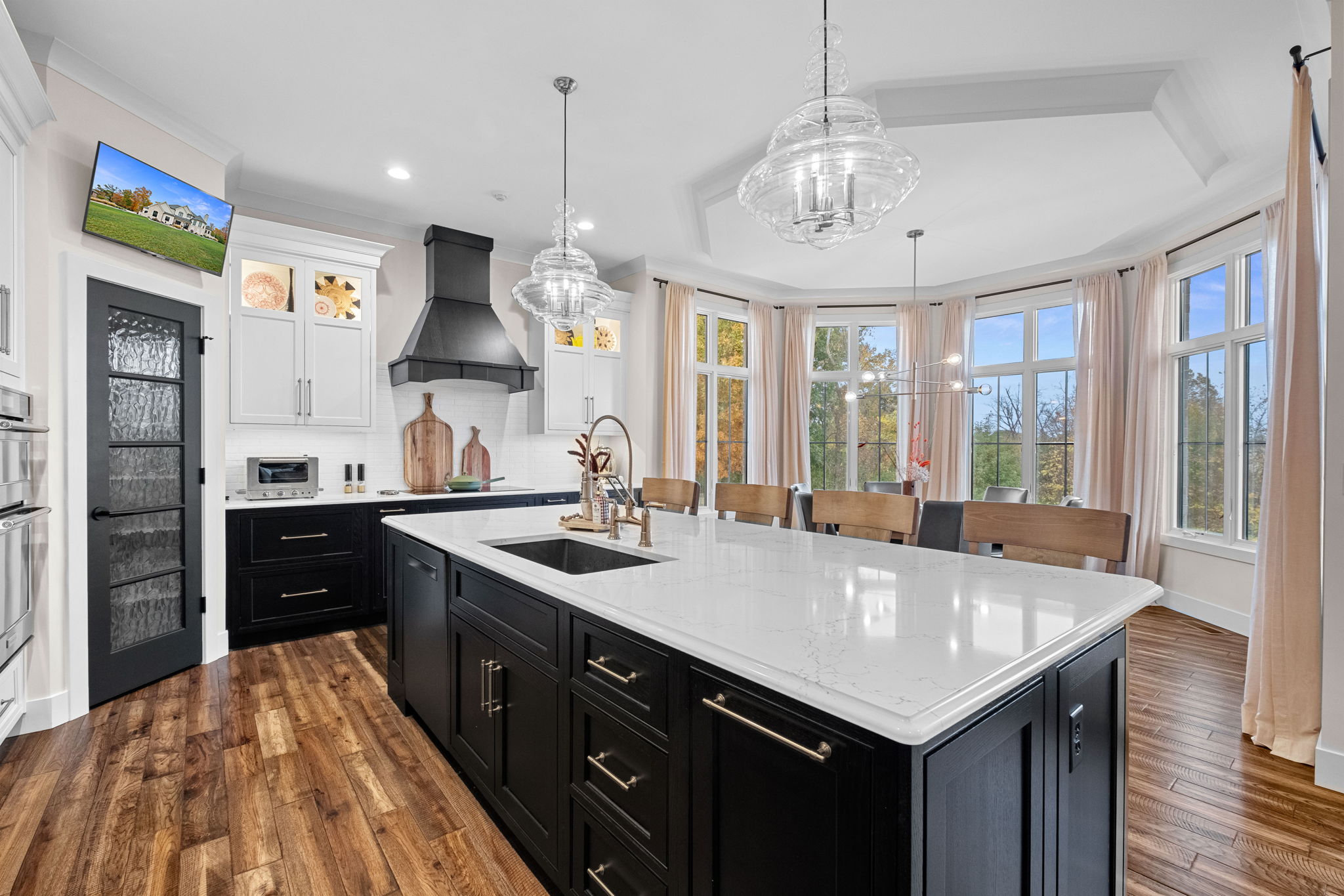 A modern kitchen featuring a large bay window, a drop ceiling, a spacious island with Cambria quartz countertops, and custom Shiloh cabinets.