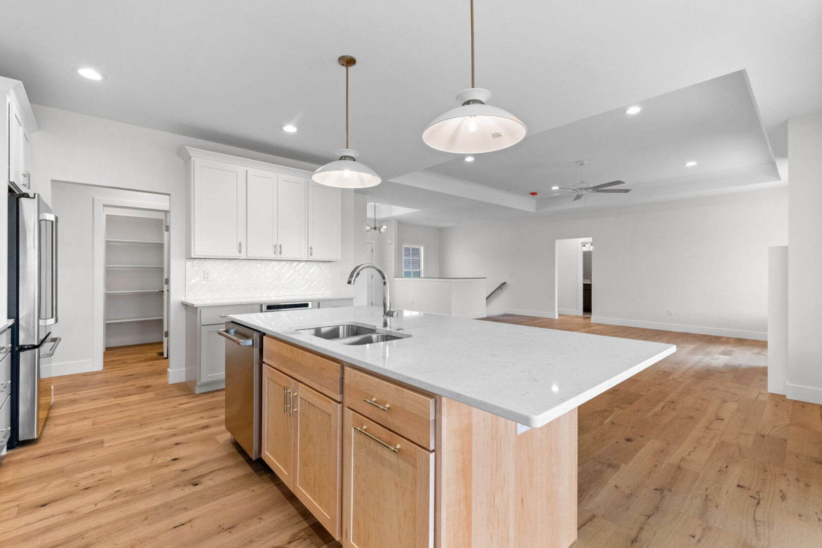 The kitchen showcases a contemporary design featuring custom Aspect cabinetry and quartz countertops, complemented by Café stainless steel appliances. It highlights a wooden bodice-shaped hood vent and modern dome lighting, all revolving around an impressive white oak island. In the great room, a tray ceiling and a fireplace with tiled surround are accentuated by a sleek, three-legged mantle.