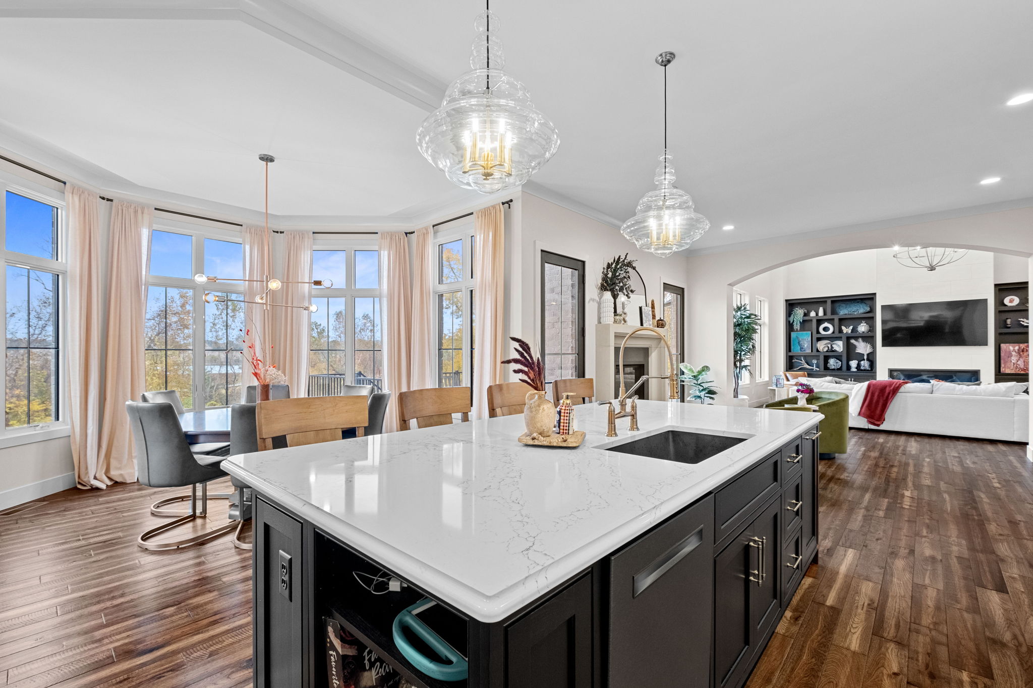 A modern kitchen featuring a large bay window, a drop ceiling, a spacious island with Cambria quartz countertops, and custom Shiloh cabinets.