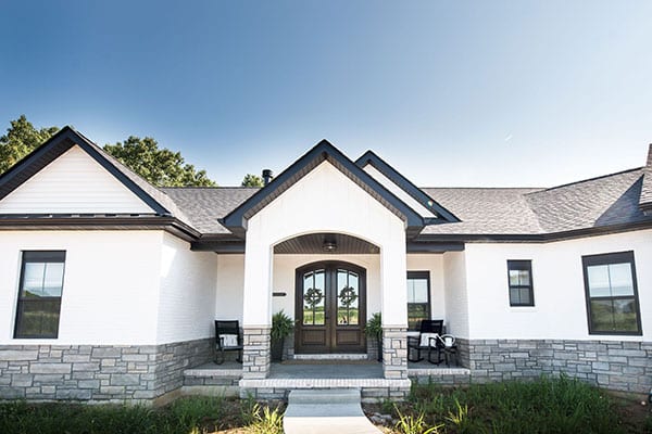 A modern farmhouse design featuring white brick and stone wainscoting, complemented by a ranch-style floor plan. Pioneer Ridge
