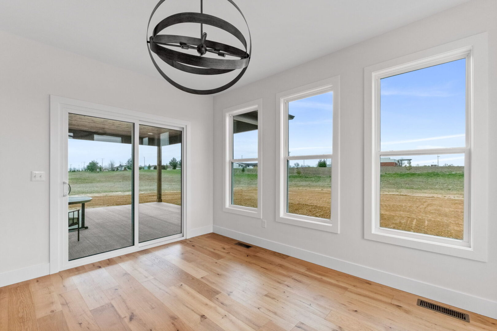 The dining room is bathed in bright natural light, complemented by a modern chandelier and engineered hardwood floors.