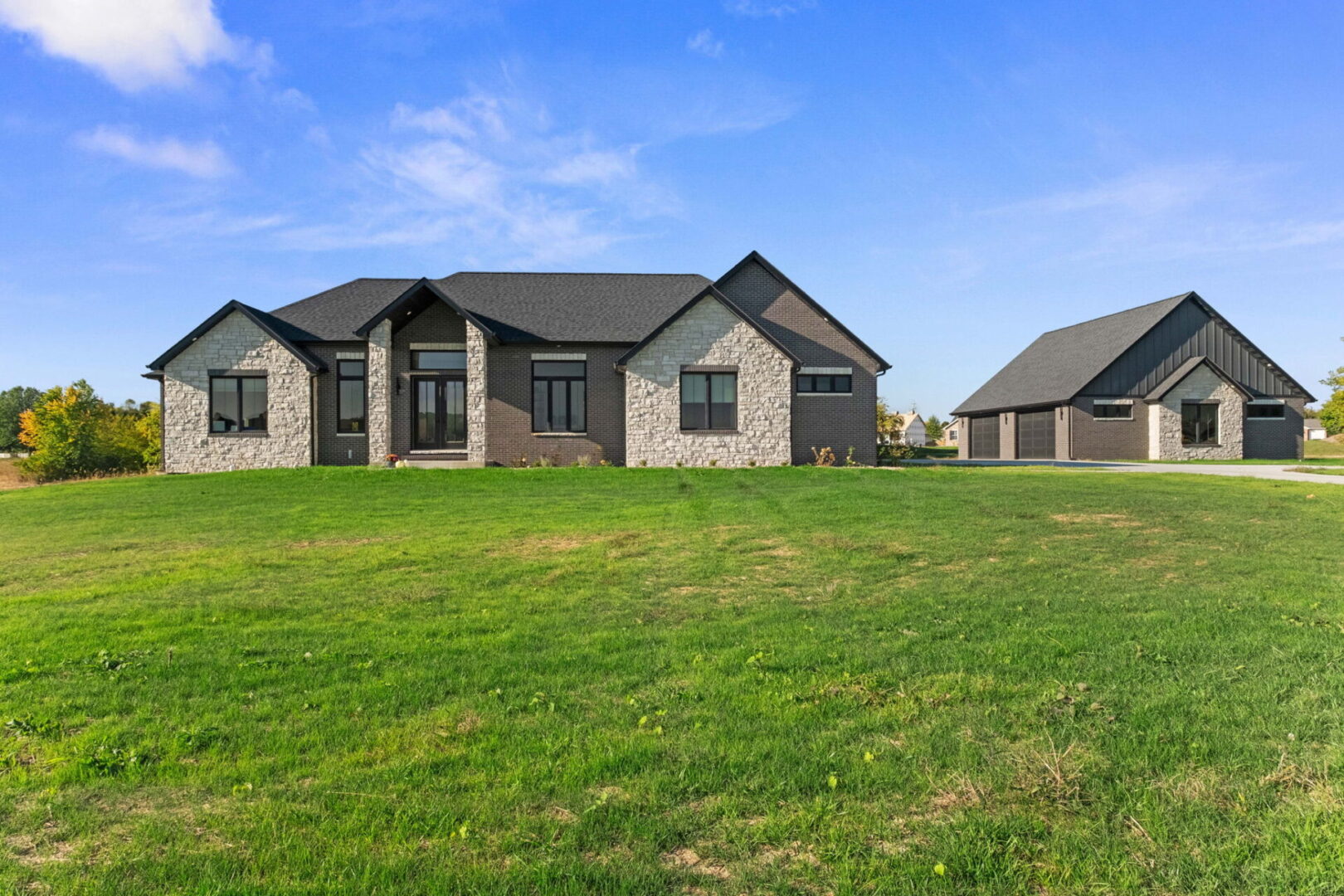 A contemporary-style home featuring black brick and stone, complete with an additional detached garage.