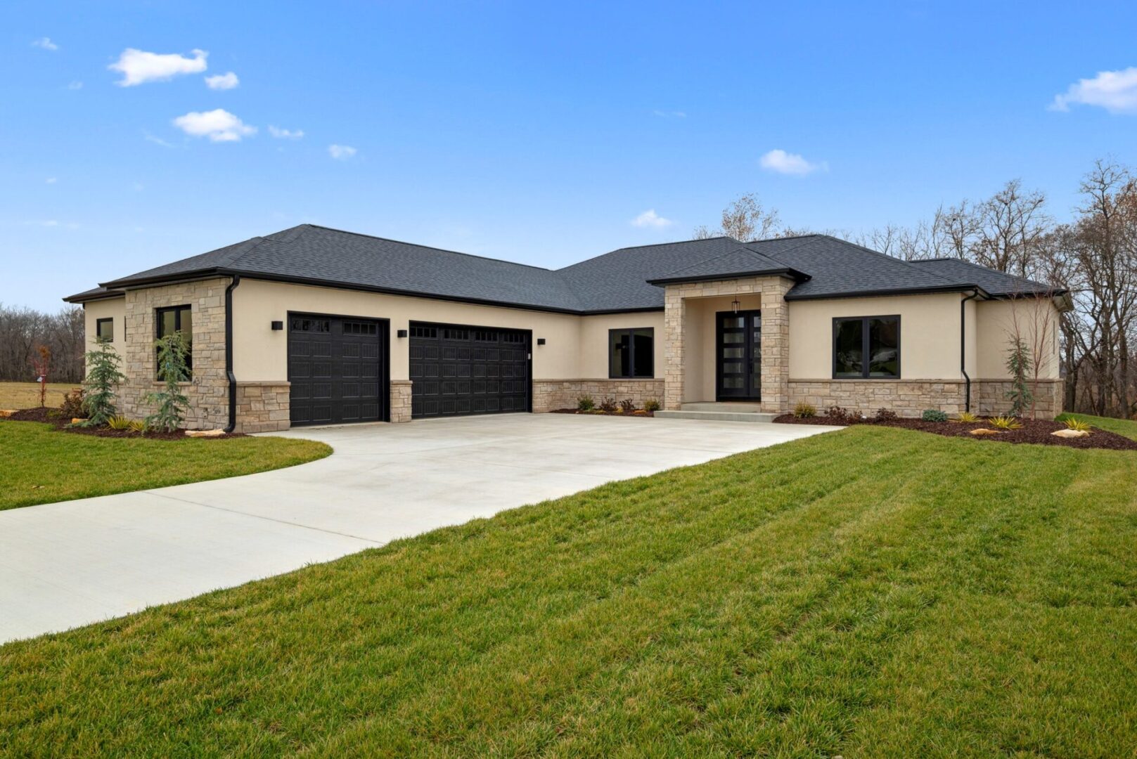 The coastal modern home in the Legacy subdivision boasts front elevations adorned with light-toned EIFS, creamy-gray stone, and dark, sultry siding, complemented by a matching stone pillar at the entryway.