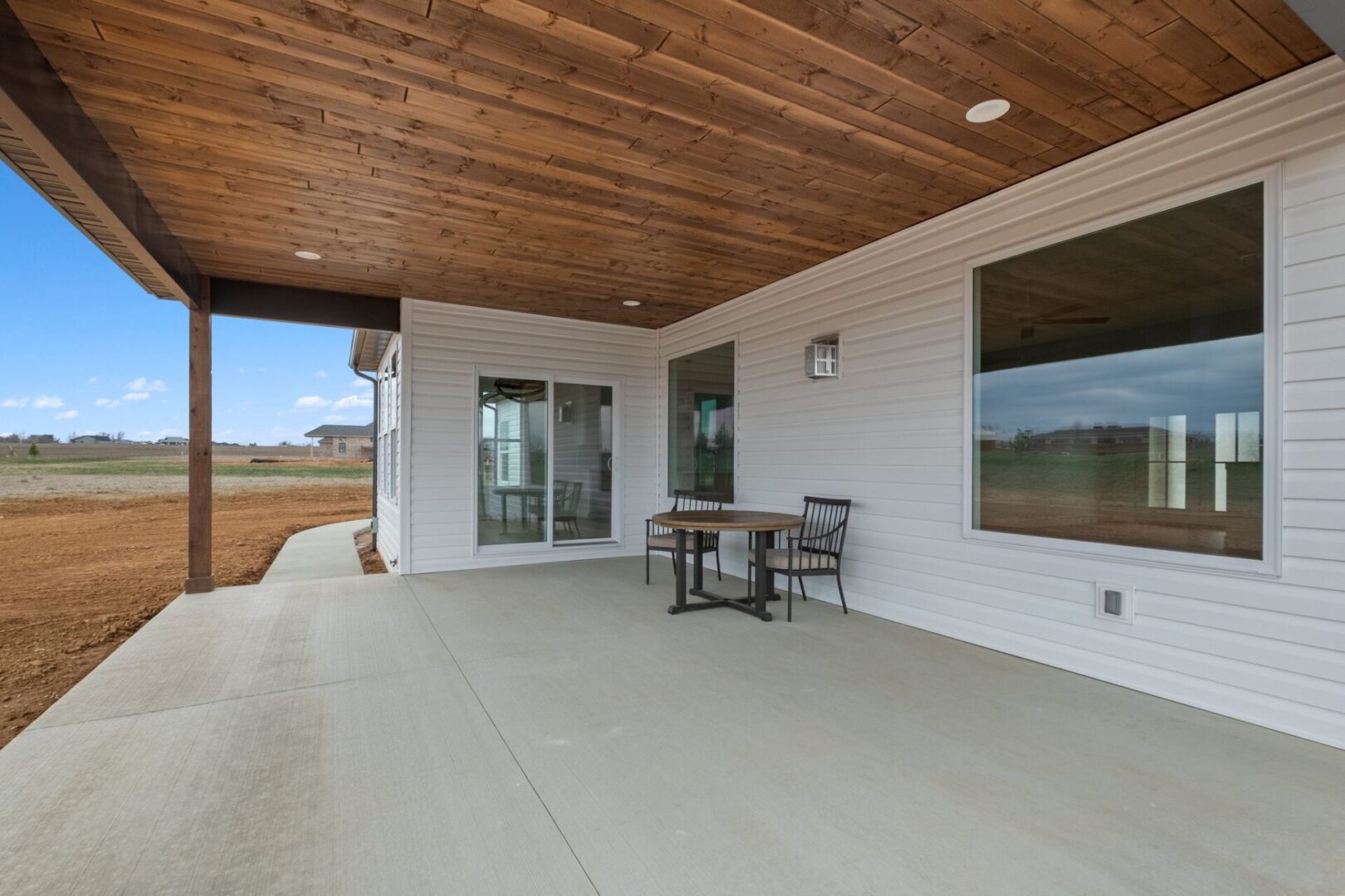 Legacy home designs featuring front and rear elevations with light toned brick exterior, creamy siding, and a stone pillar entryway. Three car garage, with 2 separate bays. Featuring the backyard and covered patio.
