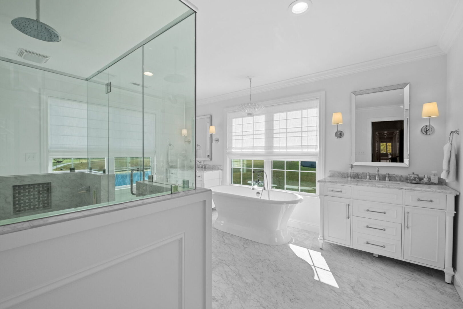A Colonial-style home boasts a classically elegant primary bathroom, complete with pristine white and marble finishes. It features double separate vanities and a spacious soaker tub that offers views of the expansive front yard.