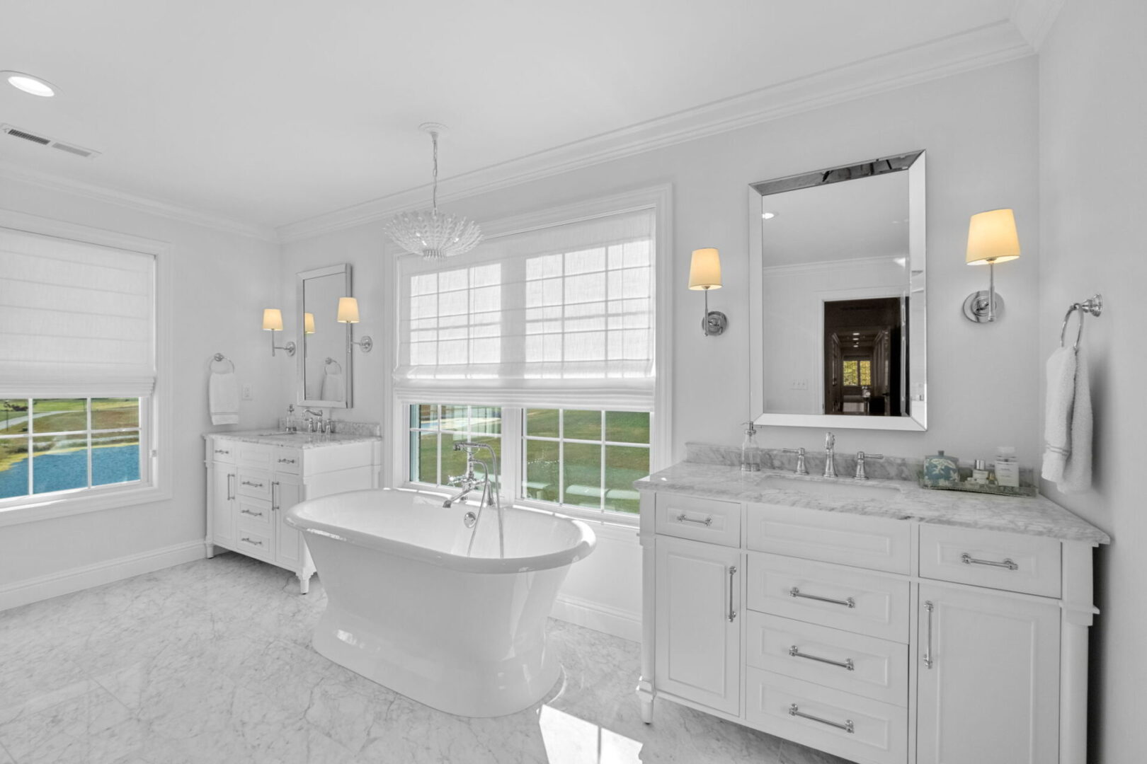 A Colonial-style home boasts a classically elegant primary bathroom, complete with pristine white and marble finishes. It features double separate vanities and a spacious walk-in shower and soaker tub.