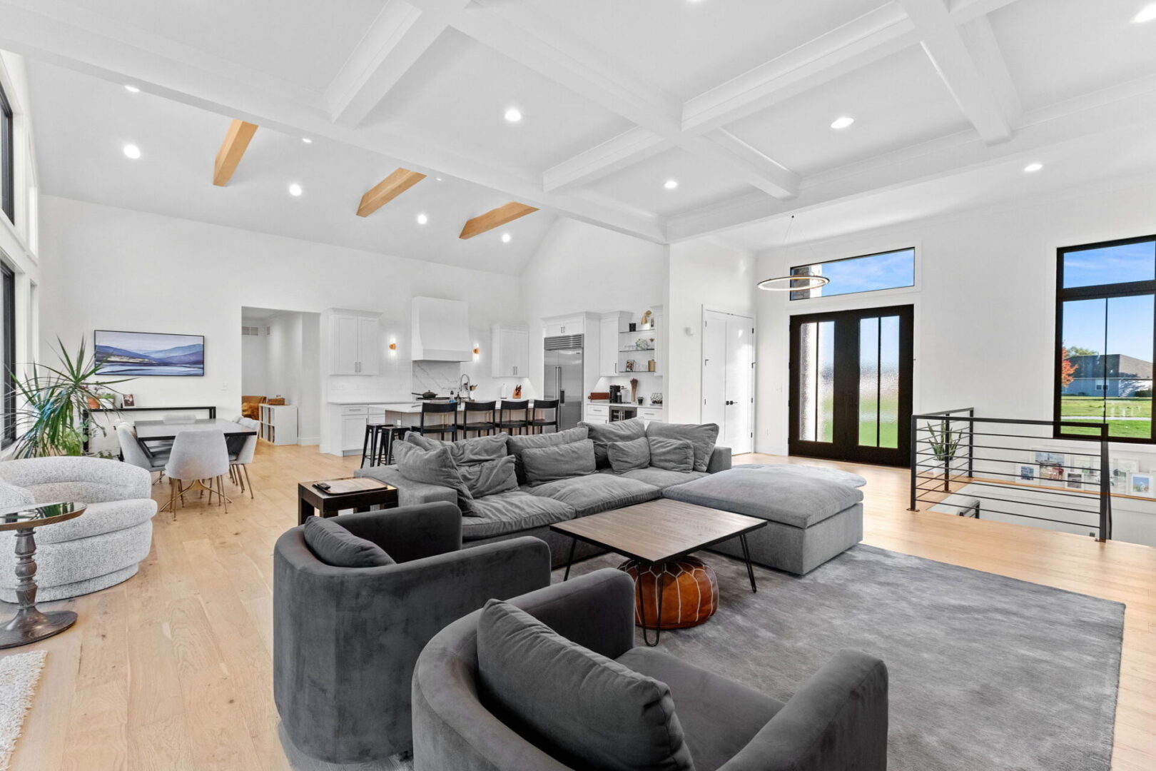 A great room with a coffered ceiling and a linear stone fireplace. Open floor plan flows into the modern kitchen.