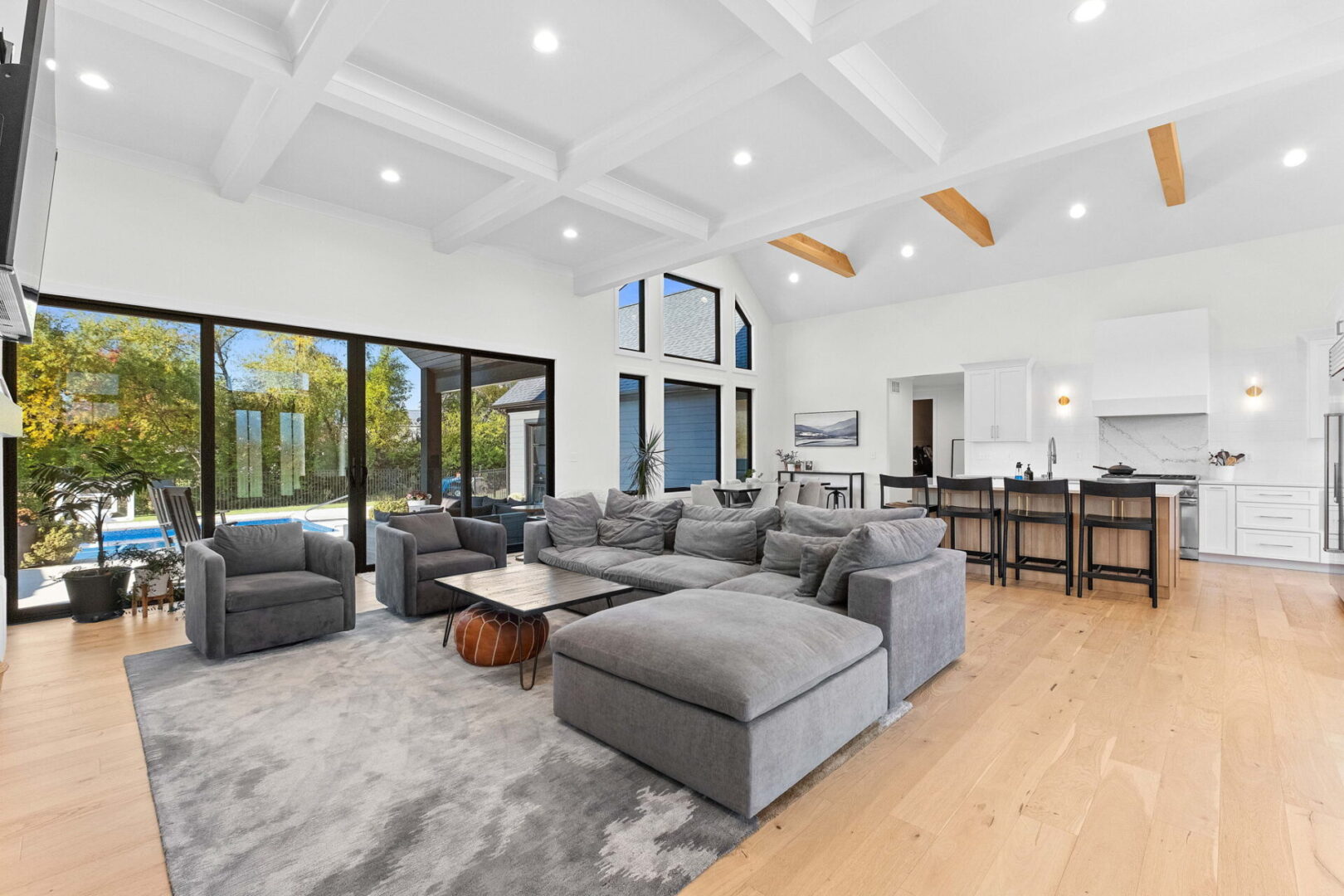 A great room with a coffered ceiling and a linear stone fireplace. Open floor plan flows into the modern kitchen.