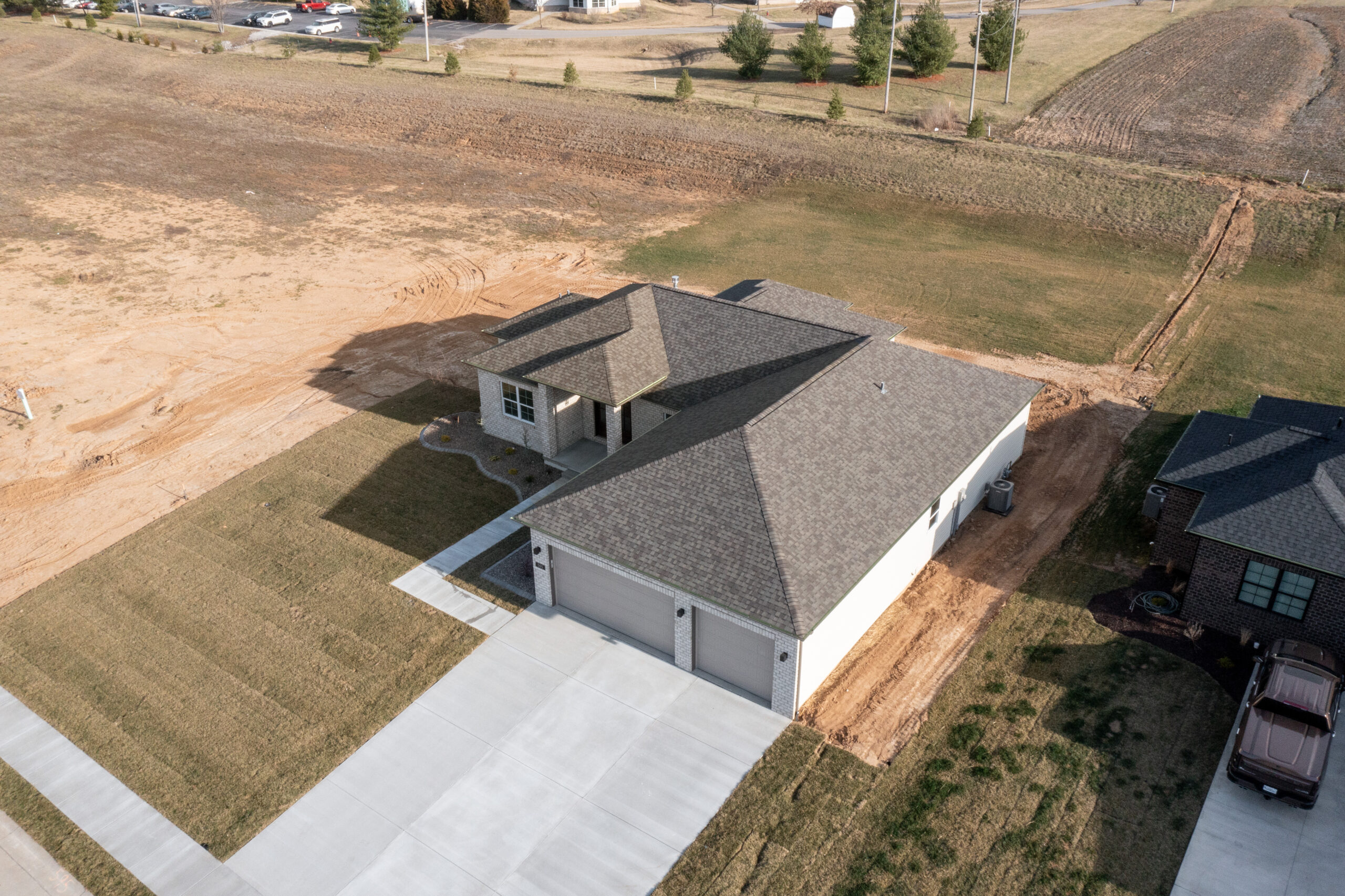 Drone photo of modern Legacy home. Legacy home designs featuring front and rear elevations with light toned brick exterior, creamy siding, and a stone pillar entryway. Three car garage, with 2 separate bays.