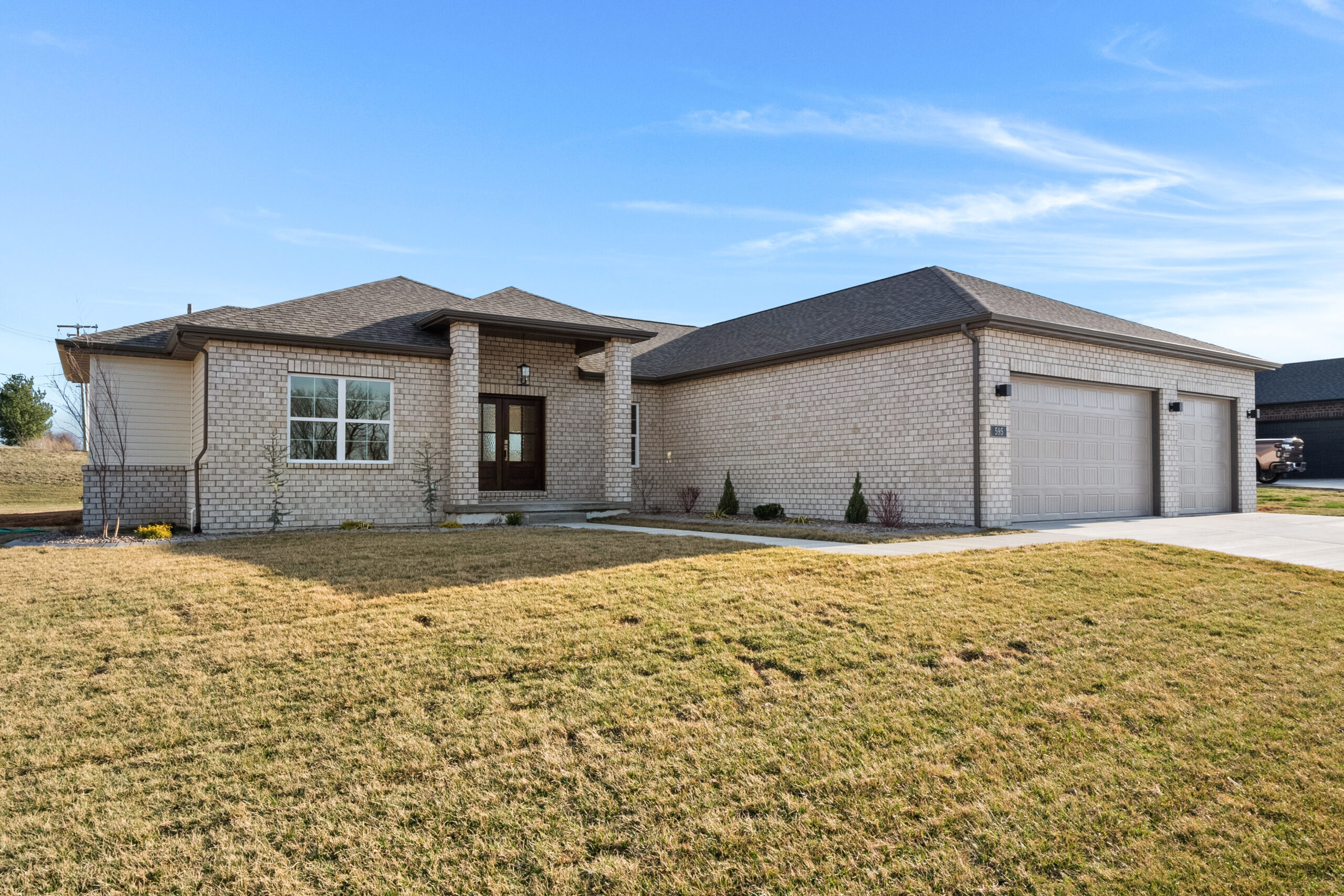 Legacy home designs featuring front and rear elevations with light toned brick exterior, creamy siding, and a stone pillar entryway. Three car garage, with 2 separate bays.