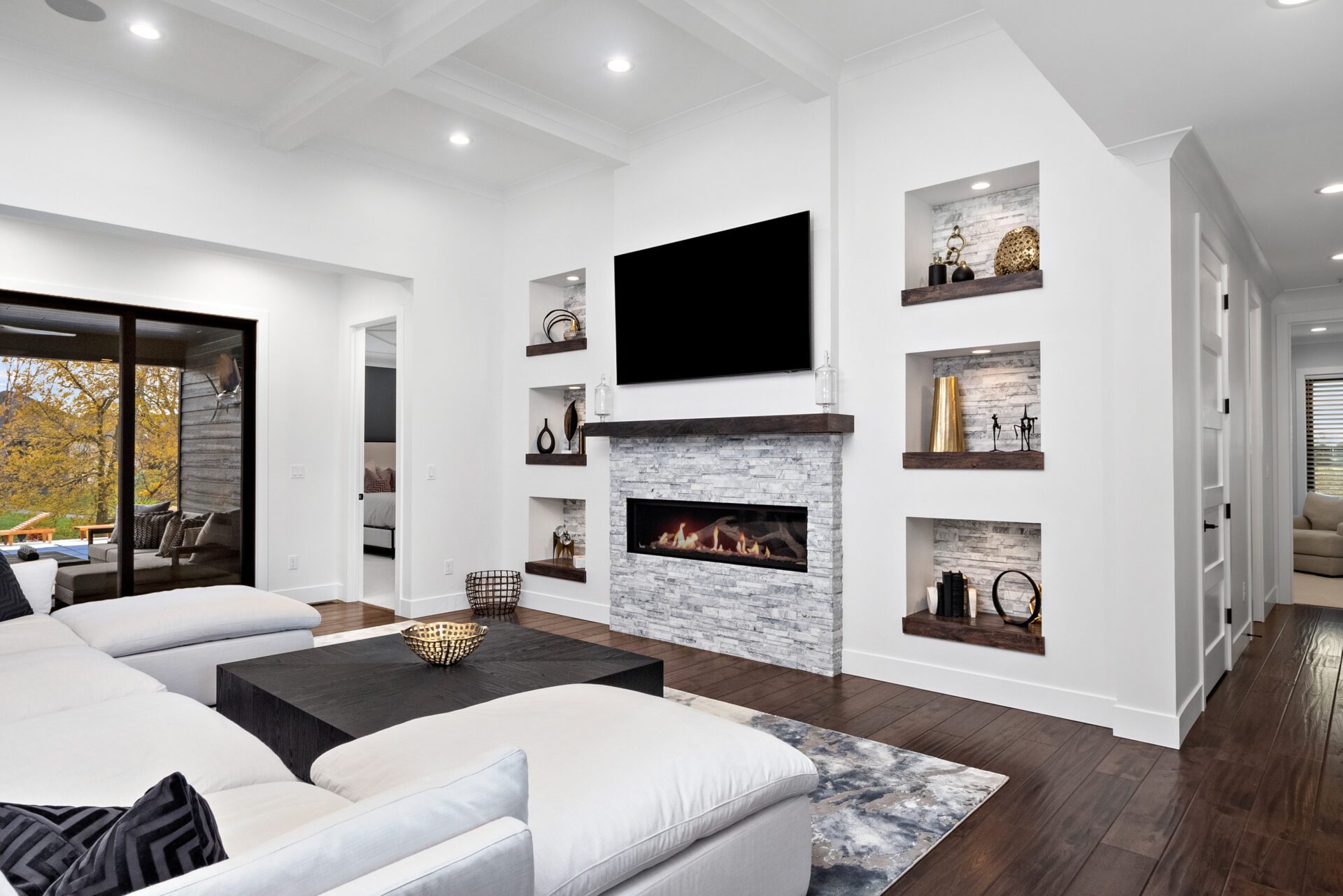 Envision a spacious, open-concept home with a contemporary modern design, boasting a coffered ceiling and wide sliding glass doors that open to a covered porch. It features elegant modern-style built-in niches and a substantial linear stone fireplace.