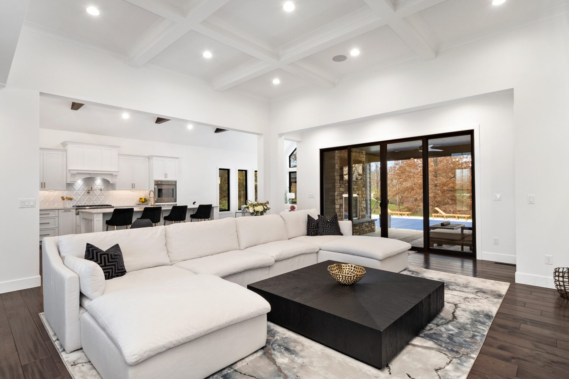 A spacious, open-concept contemporary modern design featuring a coffered ceiling and expansive sliding glass doors that lead to a covered porch.