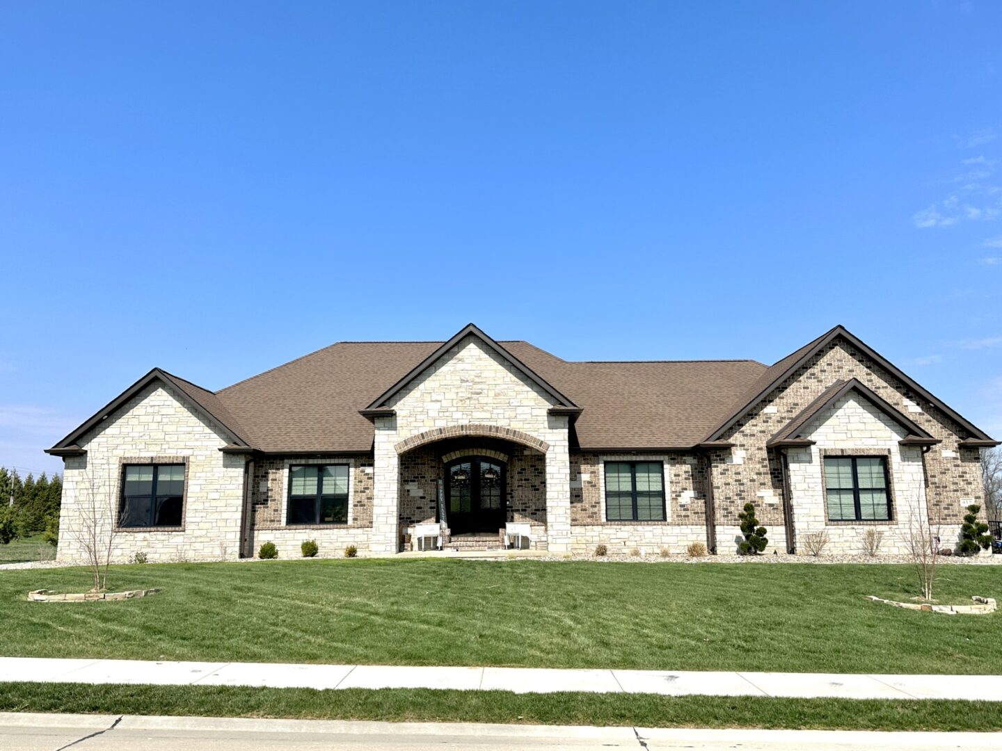 A ranch-style home featuring light-colored stone and multi-toned brick, complete with a stone archway over the double doors.